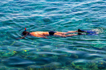 Man snorkeling with camera in hand in the sea with transparent water