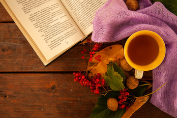 Cropped photo of a white cup with tea and a violet sweater strewn with orange maple leaves on a wooden table. The concept of comfort, coziness and hygiene. Autumn mood, fall season. Selective focus, c