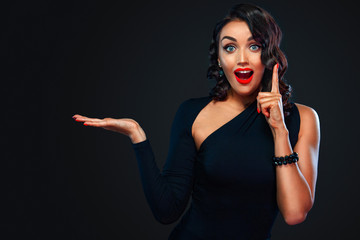 Attention and wow emotion. Black friday sale concept with beautiful girl with curly hair for shop. Happy young woman standing isolated over dark background pointing to looking left.