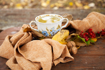 Autumn still life with cup of tea, plaid and leaves on wooden background