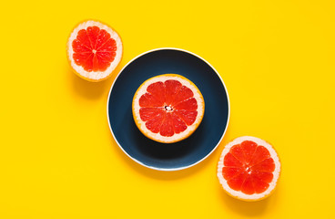 Three parts of  grapefruits on color plate on yellow background. Concept of raw vegan food. Flat lay.