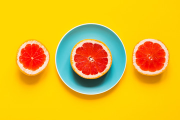 Top view - Brights fresh three parts of  grapefruits on color plate on yellow background. Concept of raw vegan food.