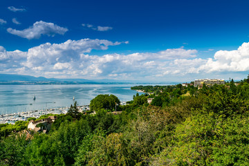 Fototapeta na wymiar Top view of the green coast and the port of Thonon les Bains, boats, Lake Geneva, and the blue sky with clouds.