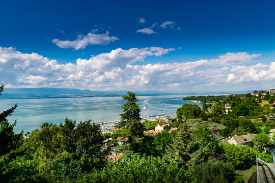 Top view of the green coast and the port of Thonon les Bains, boats, Lake Geneva, and the blue sky with clouds.