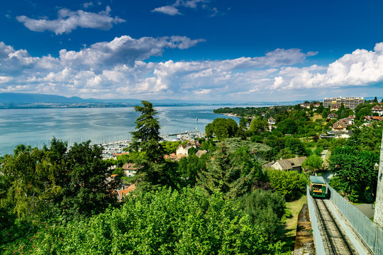 Top view of the green coast and the port of Thonon les Bains, boats, Lake Geneva, and the blue sky with clouds.