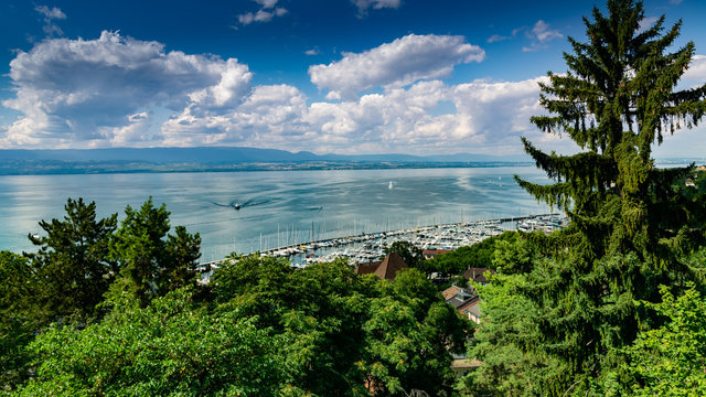 Top view of the green coast and the port of Thonon les Bains, boats, Lake Geneva, and the blue sky with clouds.
