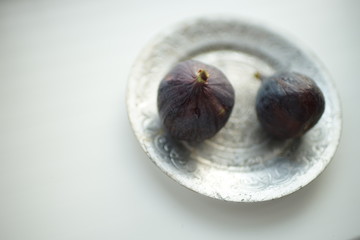 Two ripe sweet figs on a silver plate and white table. Blurred photo