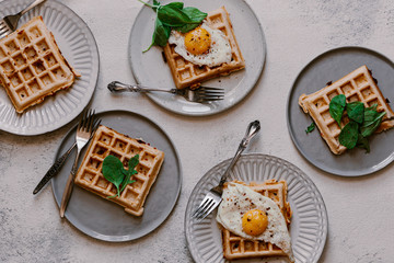 Crispy golden brown Belgian savory waffles with fried egg on top and arugula and spinach. Breakfast time on white table. Food pattern