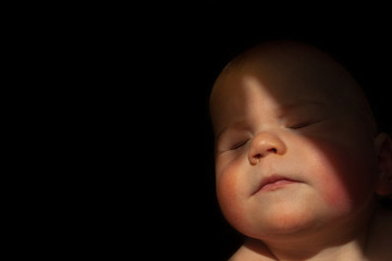 baby boy blinking into the sun with dark background