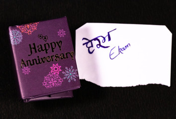 Hand written initials on white paper and happy aniversary mini message book on black background. Anniversary message concept