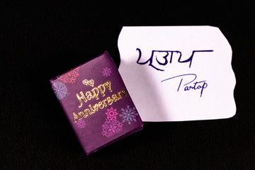 Hand written name initials on white paper and happy aniversary mini message book on dark surface....