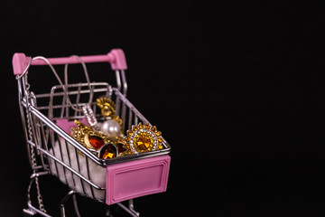 Jewellery shopping concept. Mini cart full of beautiful jewellery on black background