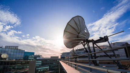 Antenne satellite sur un immeuble moderne de bureaux, ciel bleu et soleil couchant