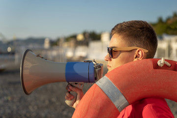 Young lifeguard with megaphone on beach background. Lifeguard on duty with a life buoy at the beach
