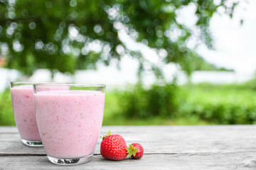 A glass of fresh cold smoothie with berries and cherrys on a wooden table, summer set, outdoor greed blured background,boke.