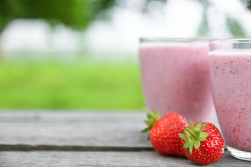 A glass of fresh cold smoothie with berries and cherrys on a wooden table, summer set, outdoor greed blured background,boke.