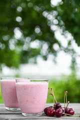 A glass of fresh cold smoothie with berries and cherrys on a wooden table, summer set, outdoor greed blured background,boke.