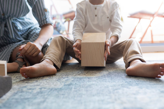 Unrecognisable toddler boy sitting on the living room floor with his mother and playing with wooden toys.
