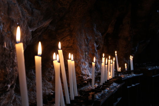 Row of lit candles on offer to the cult of the Virgin Mary (Madonna), in the cave of the sanctuary of the Mentorella, in Guadagnolo. Rome, Lazio, Italy. Sacred place of prayer, peace and silence.