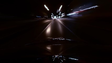 Long exposure time lapse night city from roof of moved car. Camera is mounted on roof of automobile. Reflection of light rays in windshield of auto. Theme a tunnel of neon lights and night life.