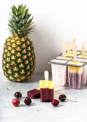 Homemade frozen popsicles of pineapple and cherry berries. Healthy summer dessert. Selective focus.