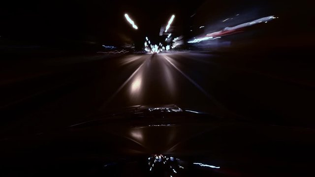 Long exposure time lapse night city from roof of moved car. Camera is mounted on roof of automobile. Reflection of light rays in windshield of auto. Theme a tunnel of neon lights and night life.