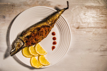 mackerel stuffed with carrots, onions and lemon and tomatoes on a white plate. Fish dishes. Wooden...