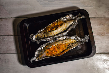 two mackerel stuffed with carrots, onions and lemon and tomatoes. Fish in foil for baking in a pan....