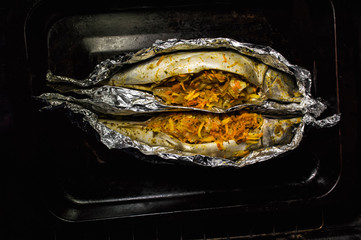 two mackerel stuffed with carrots, onions and lemon and tomatoes. Fish in foil for baking in a pan....