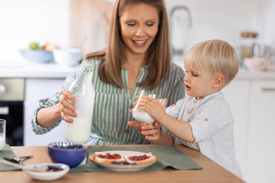 Smiling mother giving milk to her son for breakfast at home.