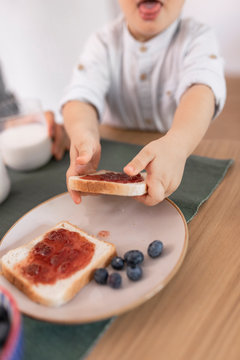 Hands of unrecognisable toddler boy holding toast with jam at breakfast.