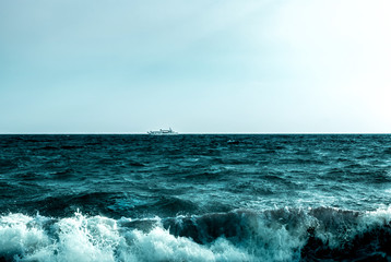 A single white ship drifting on sea horizon to the south on green stormy waves. Minimalism. Copy space