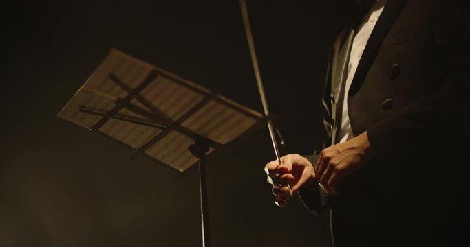 Close up shot of hands of symphony orchesra conductor directing music by waving his baton. Studio shot on black background 4k footage