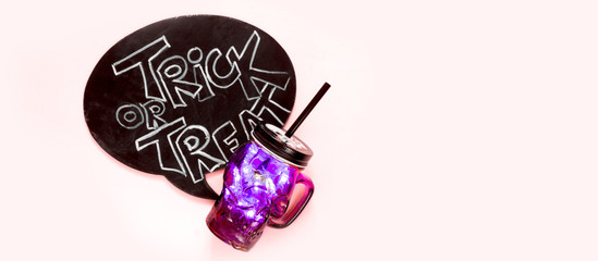 Obraz premium Halloween flat lay, woman's hand holds a glass with a skull-shaped drink and the inscription trick or treat on a pink background