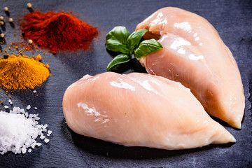 Raw chicken breasts with spices on black stone plate