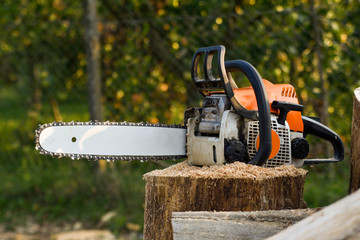  Chainsaw that stands on a heap of firewood in the yard on a beautiful background of green grass and forest.