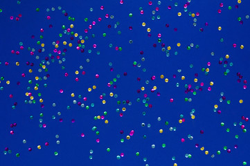 Fototapeta na wymiar Photo of confetti sparkles sprinkles on backdrop in deep blue color with shine effect. Festive holiday background for your projects. Celebration concept. Christmas pattern. Top view
