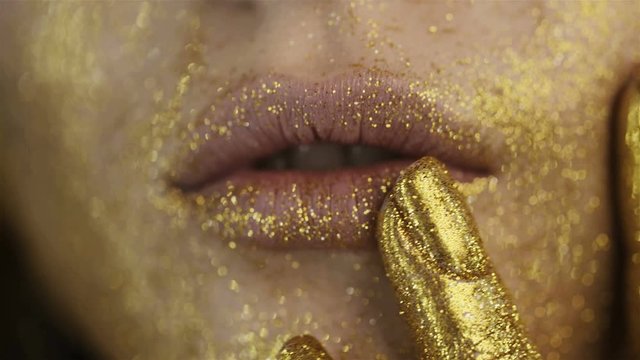 Gold lipstick. Golden makeup. Close up of beautiful lips of a girl with golden sparkles. Fingers and lips of a girl close-up. Gold paint on the face and fingers. Jewelry Advertising.