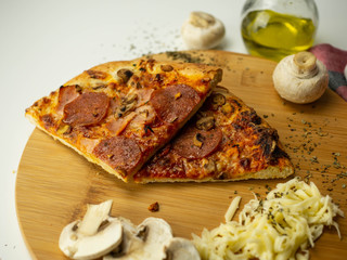 Mrożona pizza przygotowana w domu. Ser, oliwa, pieczarki, salami. Widok z góry, białe tło.