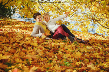mother playing with her daughter in autumn park. Mom and her child playing together on autumn walk outdoors. Happy loving family having fun.Fashion family concept - stylish mother and child wear.