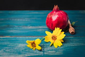 Fresh juicy pomegranate and honey stick on blue wooden table