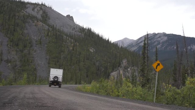 White 4x4 overland truck camper taking a curve on a dirt road in the mountains of the Canadian Arctic. Dempster Highway, Yukon.