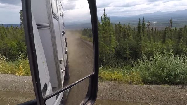 View and reflection in a mirror of a camper truck driving on a dusty dirt road. Dempster Highway, Yukon, Canada.