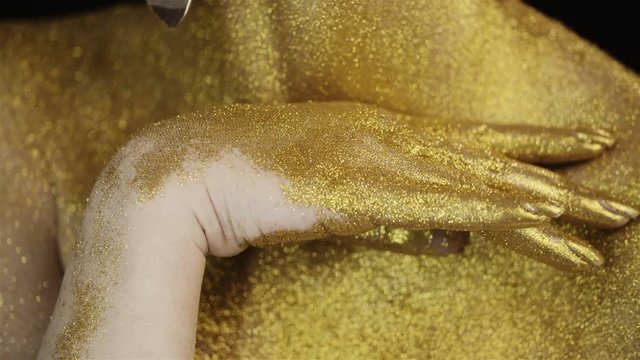 Gold glitter paint on the body girl and fingers. Body art. Girl runs a hand along her neck. Luxurious life.