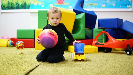 Cute little boy playing with colourful ball on soft carpet