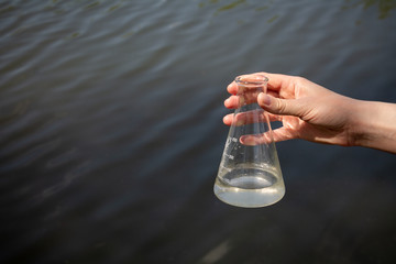 hand holding test tube for analyses with water on the background of the reservoir, the concept of water purity, pollution of water bodies, checking the quality of drinking water in cities, environment