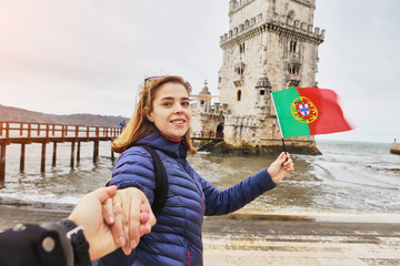 Young woman tourist walking near Belem tower holding the flag of Portugal in hands on the riverside in Lisbon