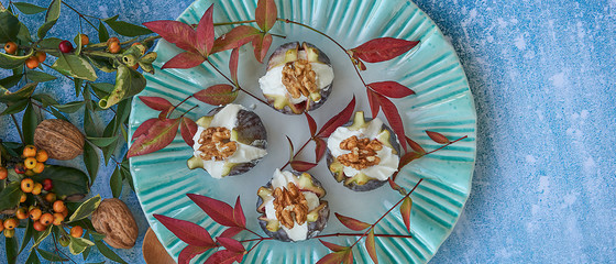 Top view. Green plate with fresh figs stuffed with cream cheese and nuts. Decoration of leaves and nuts on blue background.