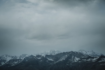Storm is coming with dark grey clouds over the horizon of the snowy peaks of the Italian Alps in bottom part of an image and bigger part of negative space in upper part