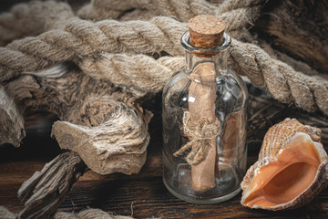 Bottle with pirate treasure map within, moorings and seashells on brown wooden table background.